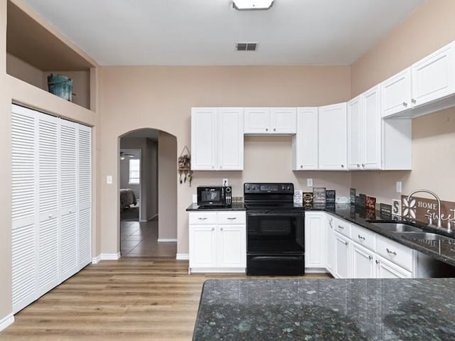 kitchen with dark stone countertops, sink, black appliances, light wood-type flooring, and white cabinets