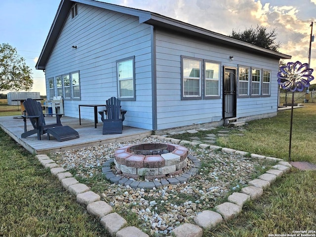 back house at dusk featuring a wooden deck, a yard, and an outdoor fire pit