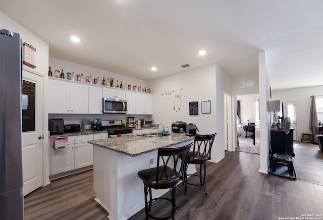 kitchen with appliances with stainless steel finishes, white cabinetry, a kitchen island with sink, and dark wood-type flooring