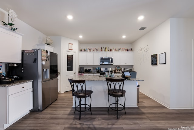 kitchen featuring dark stone counters, a center island with sink, white cabinetry, appliances with stainless steel finishes, and dark hardwood / wood-style flooring