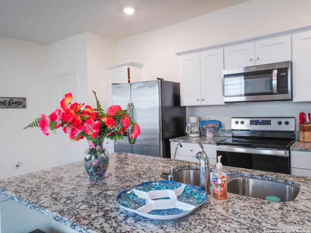 kitchen featuring appliances with stainless steel finishes, white cabinetry, light stone counters, and sink