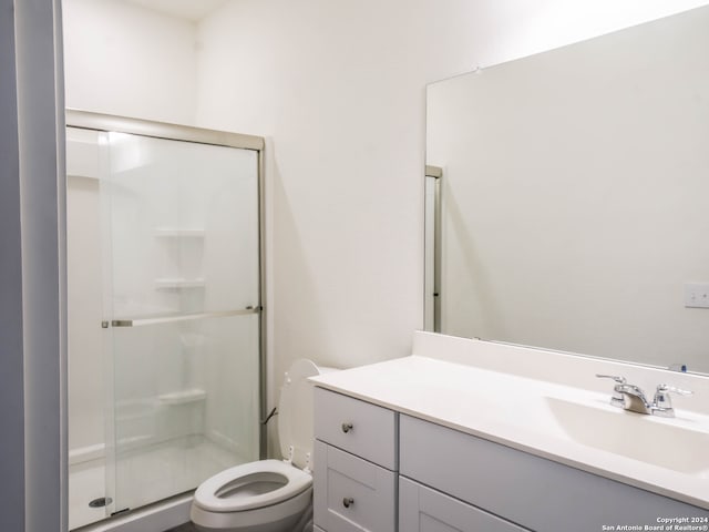 bathroom featuring toilet, vanity, and a shower with door