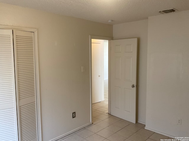 unfurnished bedroom featuring a closet, a textured ceiling, and light tile patterned floors