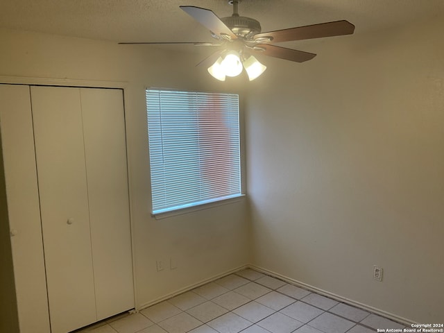 unfurnished bedroom with a closet, a textured ceiling, light tile patterned floors, and ceiling fan