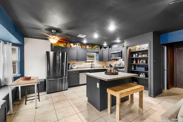 kitchen with gray cabinetry, stainless steel appliances, sink, light tile patterned floors, and a center island