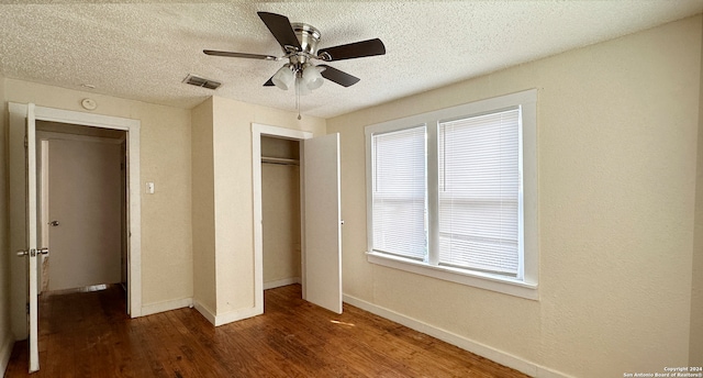 unfurnished bedroom featuring ceiling fan, a textured ceiling, multiple windows, and dark hardwood / wood-style floors