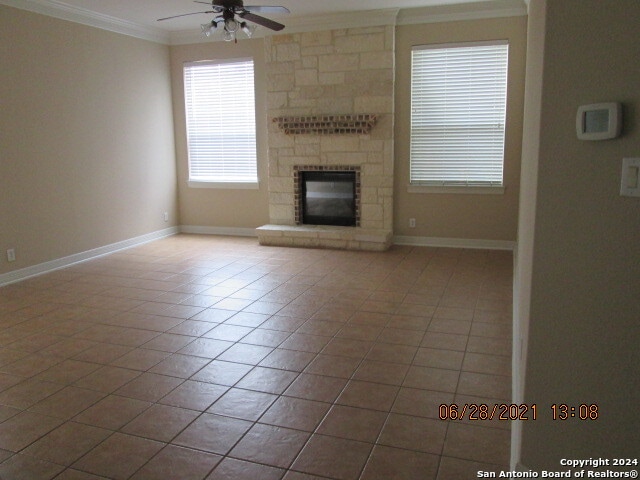 unfurnished living room featuring ornamental molding, a stone fireplace, light tile patterned floors, and ceiling fan