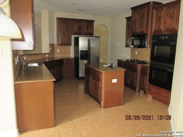 kitchen with sink, light tile patterned flooring, a kitchen island, and black appliances