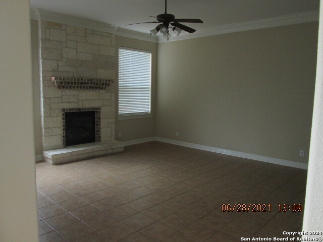 unfurnished living room with a stone fireplace, crown molding, light tile patterned floors, and ceiling fan