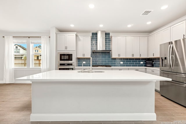 kitchen with a center island with sink, white cabinets, wall chimney range hood, light hardwood / wood-style floors, and stainless steel appliances