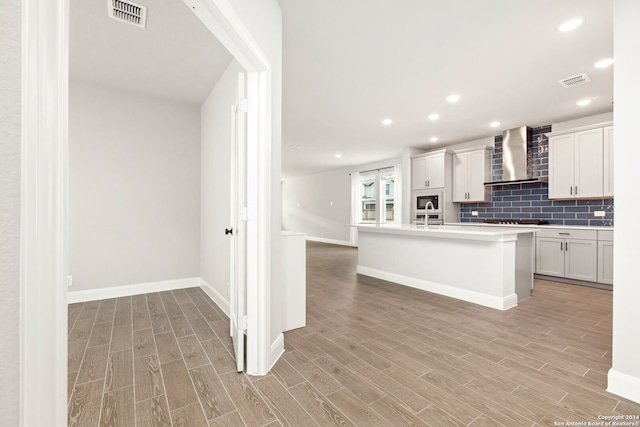 kitchen with white cabinets, an island with sink, light hardwood / wood-style floors, and wall chimney range hood