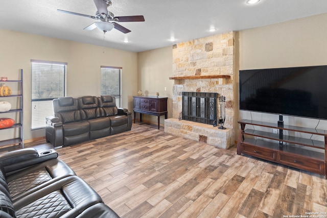 living room with a stone fireplace, light hardwood / wood-style flooring, a textured ceiling, and ceiling fan