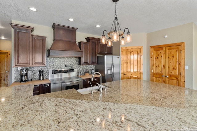 kitchen featuring light stone countertops, appliances with stainless steel finishes, decorative light fixtures, and premium range hood