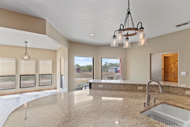 kitchen featuring sink, light stone countertops, decorative light fixtures, an inviting chandelier, and a textured ceiling