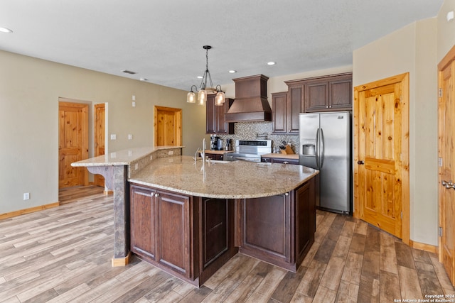 kitchen with appliances with stainless steel finishes, a spacious island, custom range hood, and light hardwood / wood-style floors