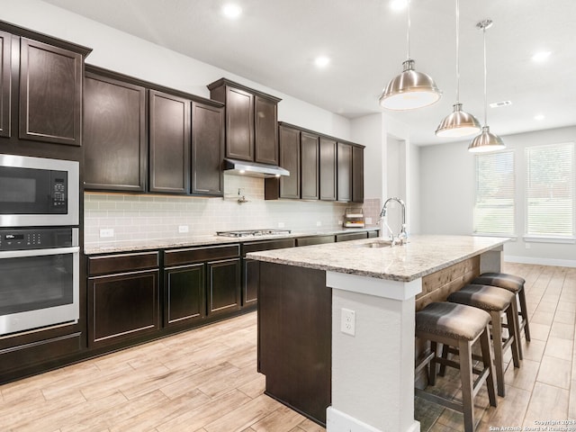 kitchen featuring a kitchen island with sink, sink, dark brown cabinetry, pendant lighting, and appliances with stainless steel finishes