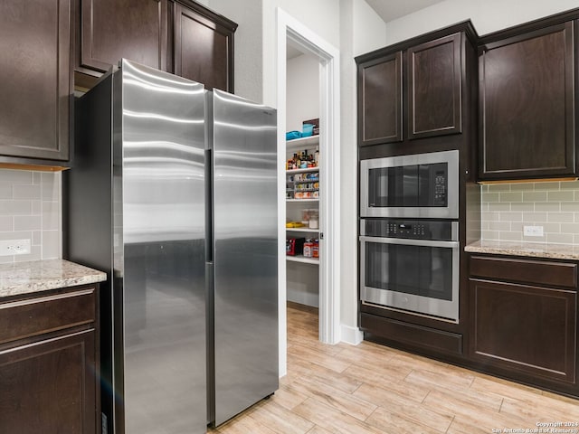 kitchen featuring appliances with stainless steel finishes, light stone counters, dark brown cabinets, and tasteful backsplash