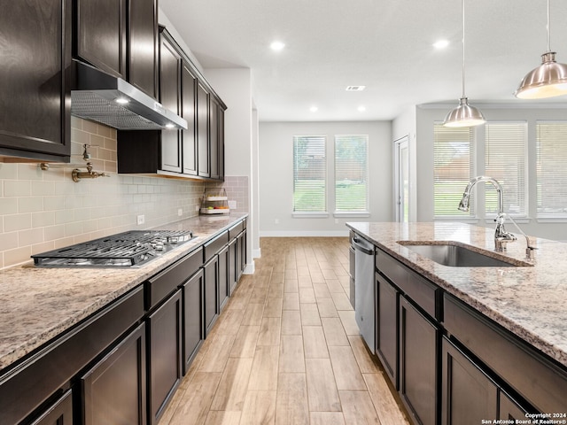 kitchen with stainless steel appliances, sink, light stone countertops, dark brown cabinetry, and decorative light fixtures