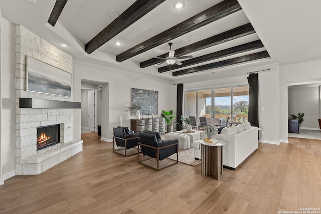 living room featuring a stone fireplace, light hardwood / wood-style flooring, beam ceiling, and ceiling fan