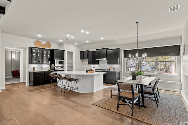 kitchen with decorative backsplash, a chandelier, light wood-type flooring, and a kitchen island with sink