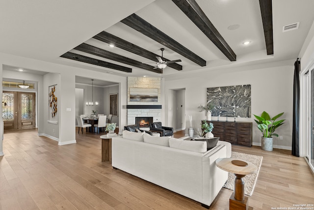 living room featuring a fireplace, beamed ceiling, light wood-type flooring, and ceiling fan with notable chandelier