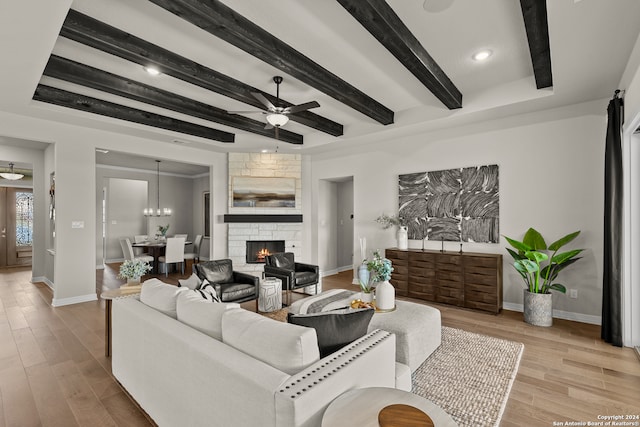 living room with a stone fireplace, light hardwood / wood-style flooring, beamed ceiling, and ceiling fan with notable chandelier