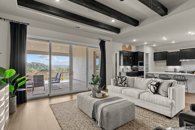 living room featuring beam ceiling, sink, and light hardwood / wood-style flooring