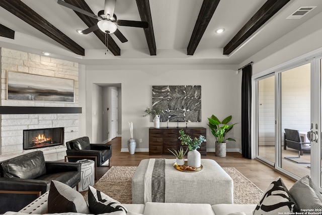 living room featuring ceiling fan, a stone fireplace, beamed ceiling, and hardwood / wood-style floors