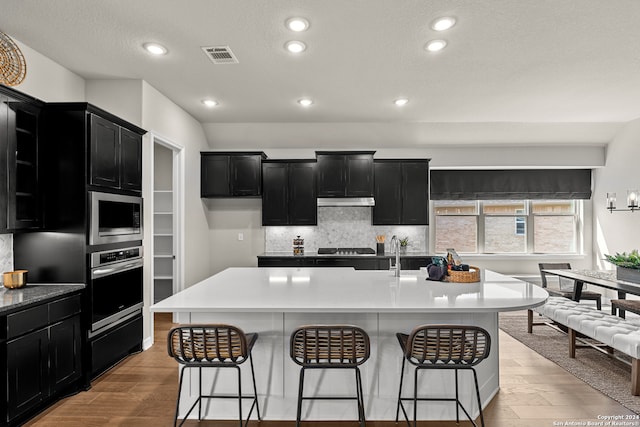 kitchen with light hardwood / wood-style flooring, a kitchen island with sink, stainless steel appliances, and a breakfast bar