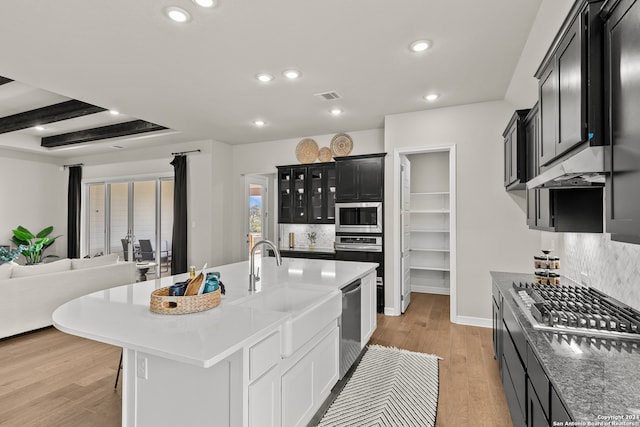 kitchen featuring decorative backsplash, an island with sink, sink, light wood-type flooring, and appliances with stainless steel finishes