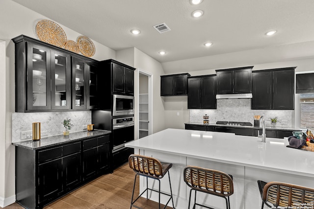 kitchen with tasteful backsplash, light stone counters, a kitchen breakfast bar, light hardwood / wood-style floors, and stainless steel appliances