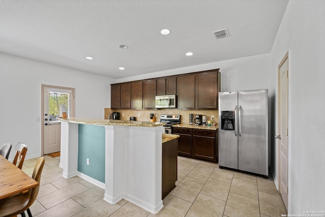 kitchen with backsplash, an island with sink, light stone countertops, dark brown cabinetry, and stainless steel appliances