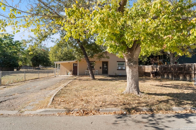 view of front facade with fence, dirt driveway, stucco siding, and an attached carport