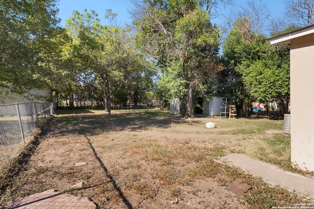 view of yard with fence, a storage unit, central AC unit, and an outbuilding