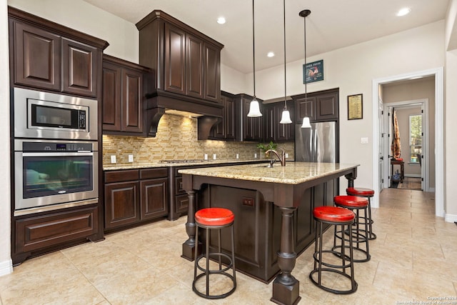 kitchen with light stone countertops, stainless steel appliances, pendant lighting, a breakfast bar area, and a kitchen island with sink