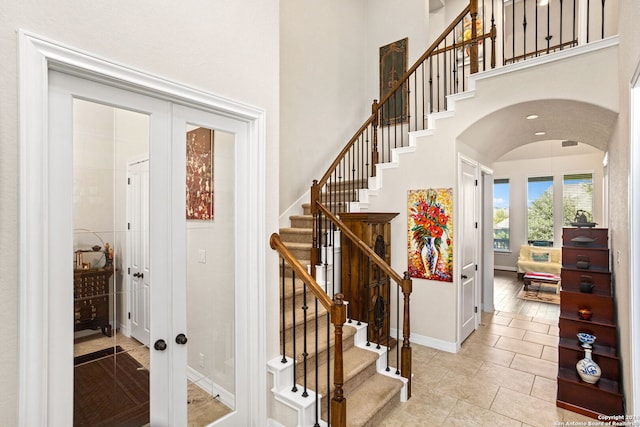 staircase featuring a towering ceiling, french doors, and hardwood / wood-style floors