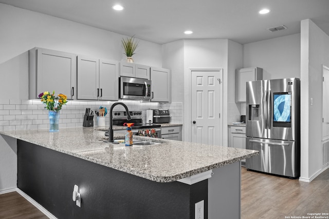 kitchen with appliances with stainless steel finishes, light wood-type flooring, kitchen peninsula, gray cabinets, and decorative backsplash