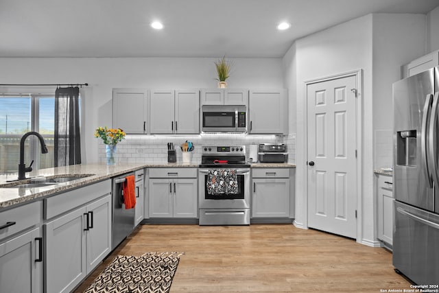 kitchen with light stone countertops, sink, light hardwood / wood-style flooring, and stainless steel appliances