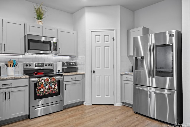 kitchen featuring gray cabinets, tasteful backsplash, stainless steel appliances, and light wood-type flooring