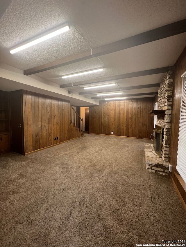 basement featuring a stone fireplace, carpet flooring, a textured ceiling, and wooden walls