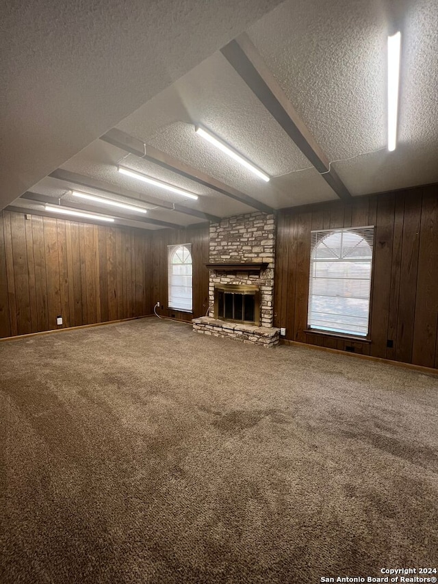 unfurnished living room with a stone fireplace, a textured ceiling, carpet floors, and wood walls