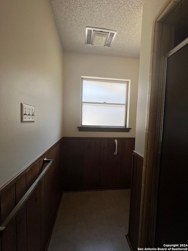 hall featuring a textured ceiling and wooden walls