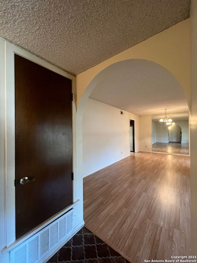 spare room with a textured ceiling, hardwood / wood-style flooring, and a chandelier