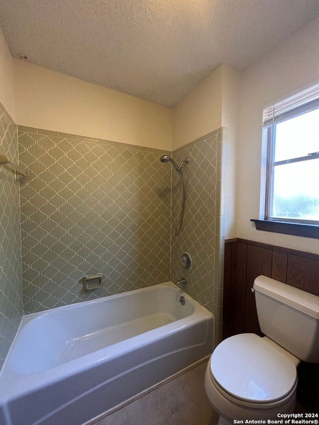 bathroom featuring toilet, wood walls, tiled shower / bath combo, and a textured ceiling