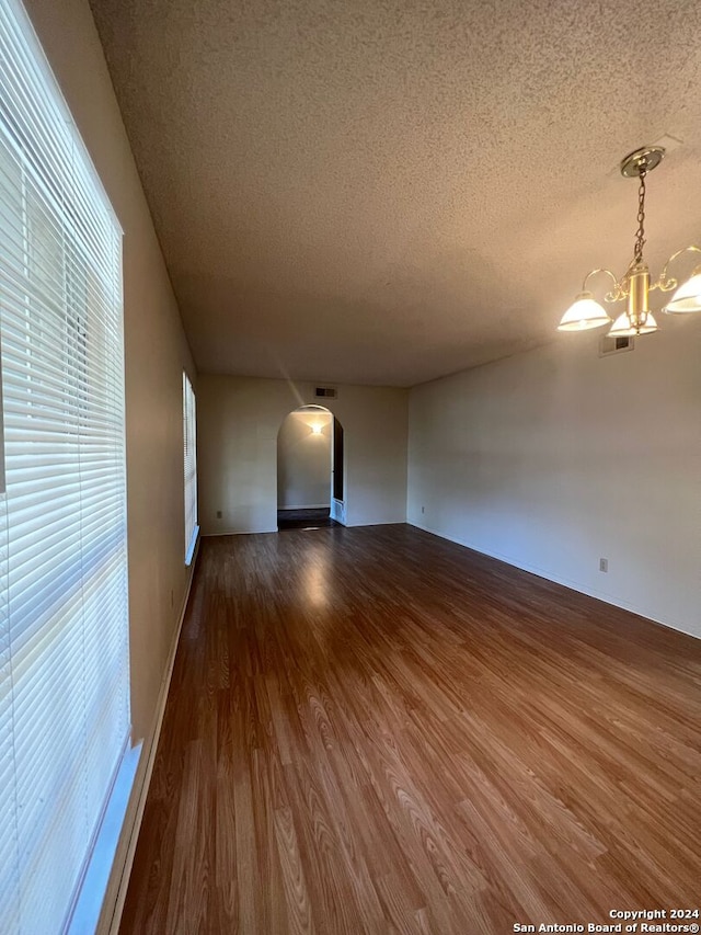 empty room with a healthy amount of sunlight, a textured ceiling, dark hardwood / wood-style floors, and a chandelier