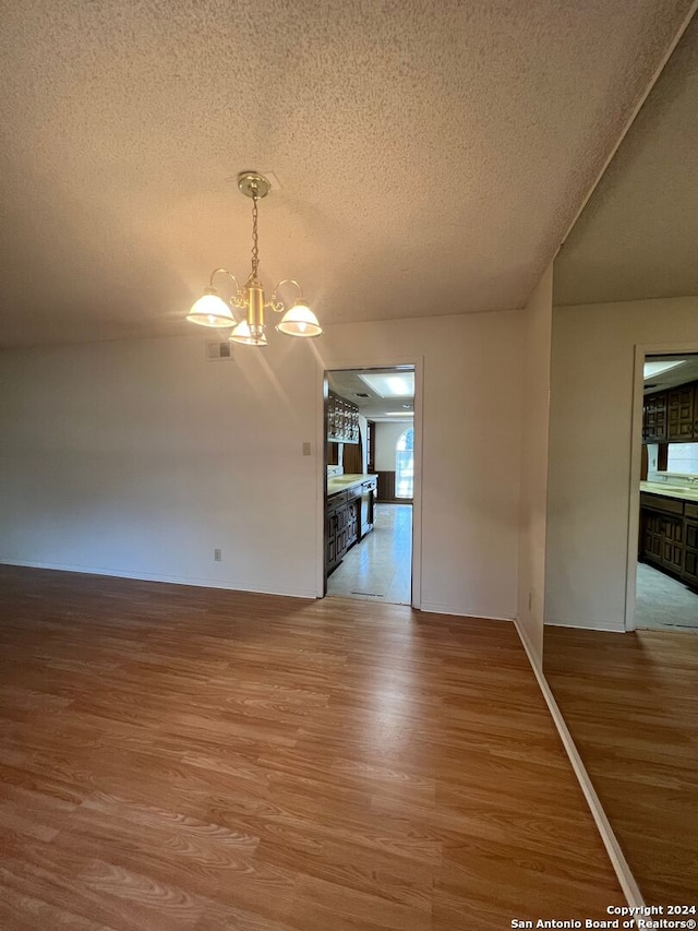 unfurnished dining area featuring an inviting chandelier, hardwood / wood-style floors, a textured ceiling, and a wealth of natural light