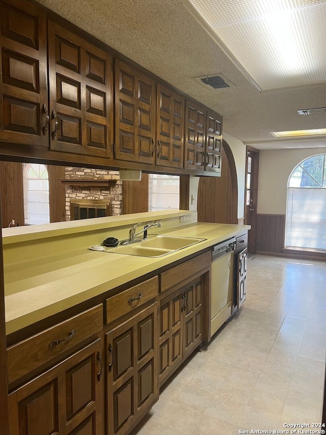 kitchen featuring dark brown cabinets, a textured ceiling, dishwasher, wooden walls, and sink