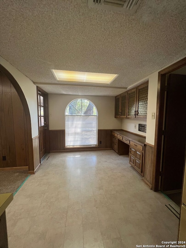 kitchen featuring built in desk, wooden walls, and a textured ceiling