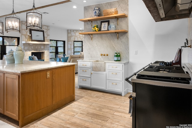 kitchen with a stone fireplace, pendant lighting, white cabinets, stainless steel range oven, and light hardwood / wood-style floors