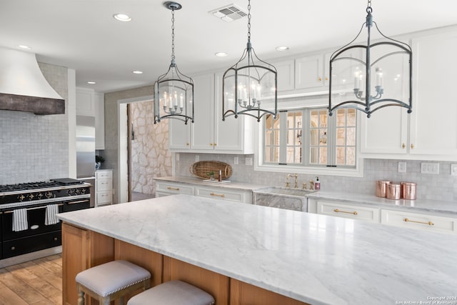 kitchen featuring light hardwood / wood-style flooring, white cabinets, custom range hood, and light stone counters